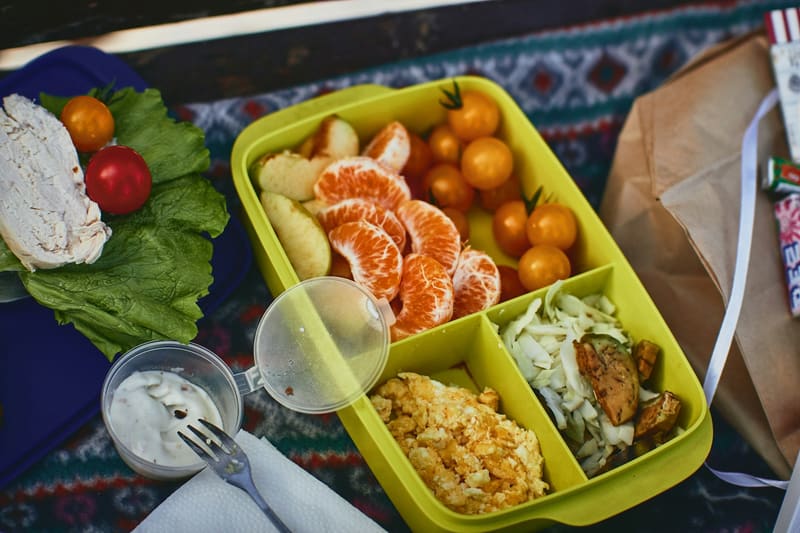 Bunte Lunchbox mit Mandarinen, Gemüse, Reis und Beeren auf einer bunten Decke
